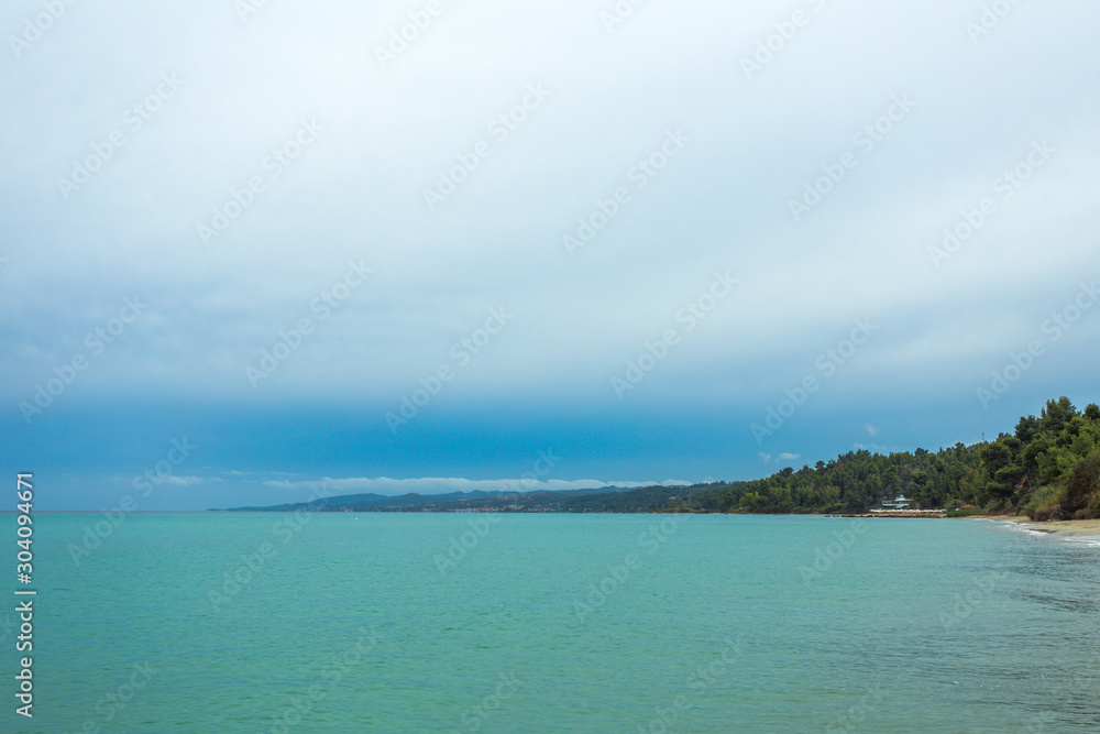 Beautiful coastal line with fresh growing green trees and blue sky and sea water landscape. Greece nature. Horizontal color photography.