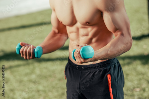 cropped shot of man exercising with dumbbells in the park