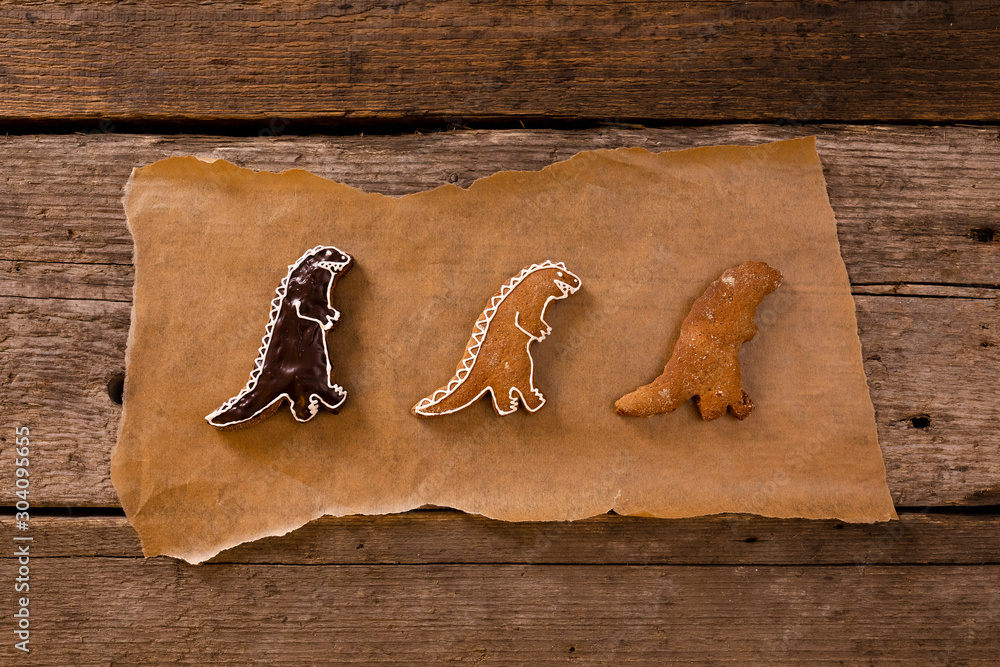 Homemade gingerbread in shapes of dinosaurs on brown baking paper on old wooden background.