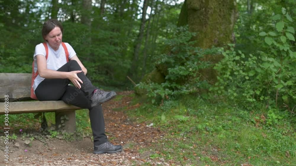 Female hiker resting on park bench and massaging leg Female hiker resting on park bench and massaging leg