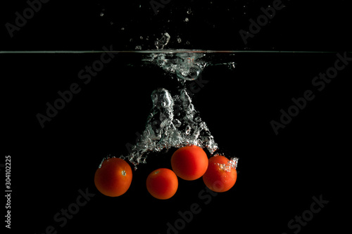 Four small tomatoes falls under water with splash