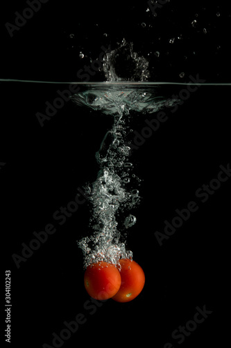 Two small tomatoes falls under water with splash 