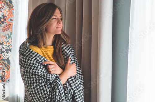 At the window stands a woman with a warm plaid. Autumn-winter time.