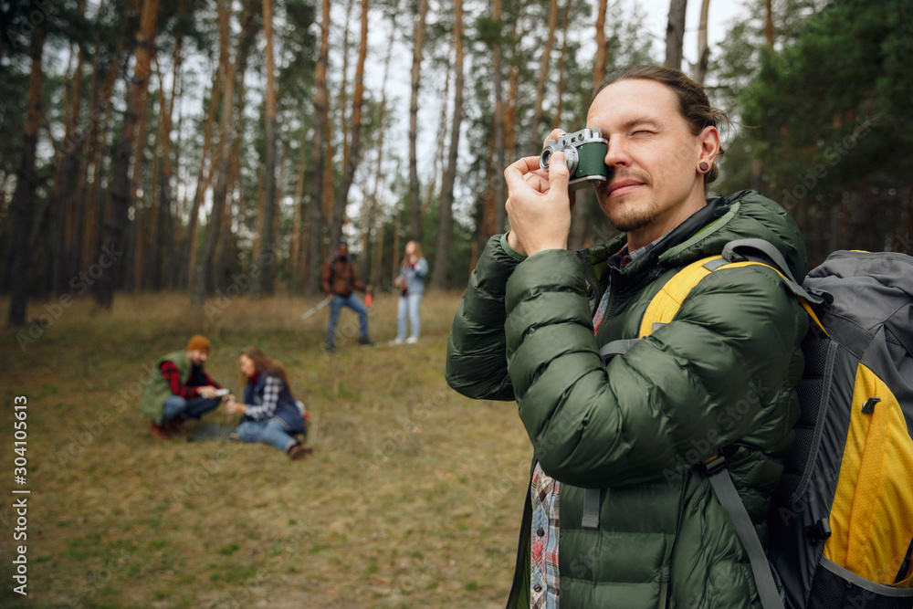 Fototapeta premium Group of friends on a camping or hiking trip in autumn day. Men and women with touristic backpacks going throught the forest, talking, laughting. Leisure activity, friendship, weekend.