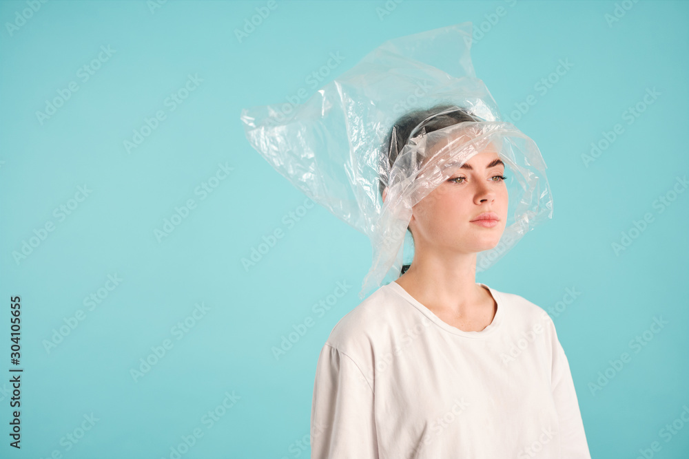 Side view of upset girl with plastic bag on head intently looking away over colorful background isolated Side view of upset girl with plastic bag on head intently looking away over colorful background isolated