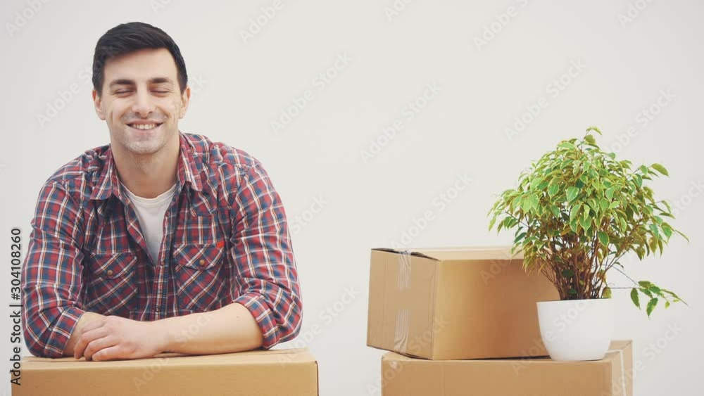 Young man standing in his new apartments, leaning on the pile of carton boxes, smiling,taking from the pocket keys to new house. Young man standing in his new apartments, leaning on the pile of carton boxes, smiling,taking from the pocket keys to new house.