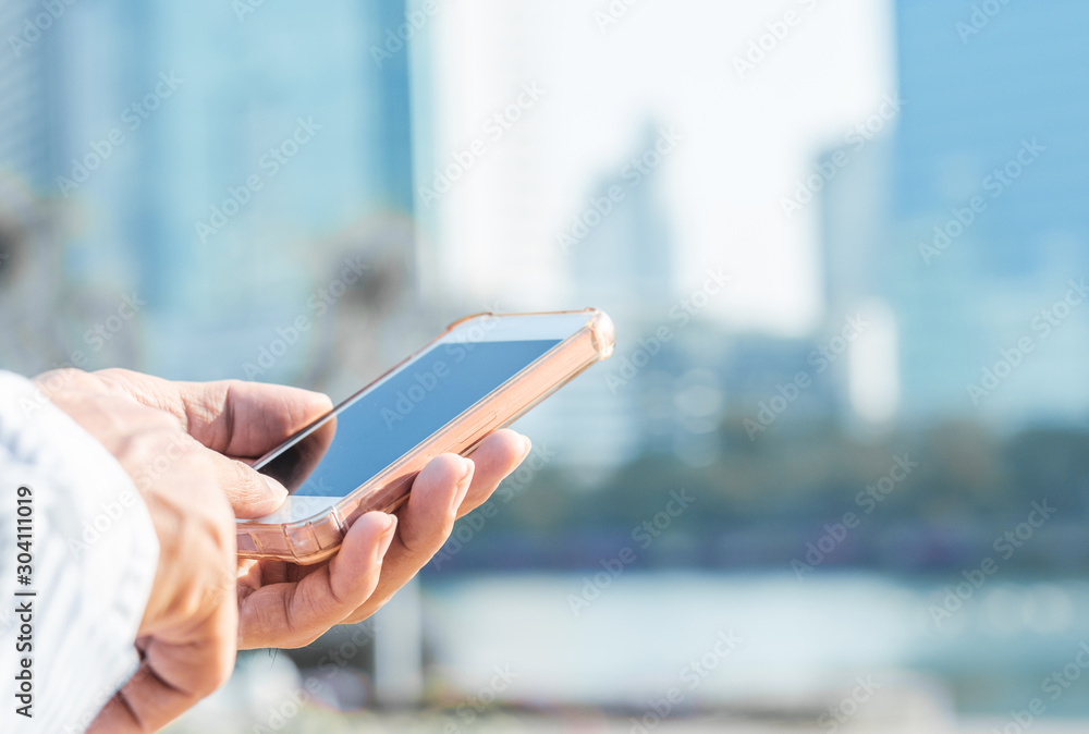 close up handsome man using hand typing smartphones and touch screen working search with app devices outdoor in city with sunrise and building background. 5G technology connecting the world.