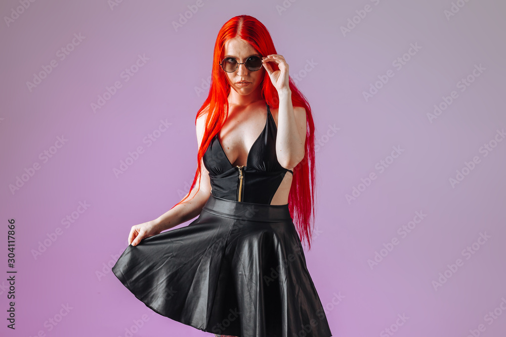 Girl with red long hair in round glasses leather skirt on pink