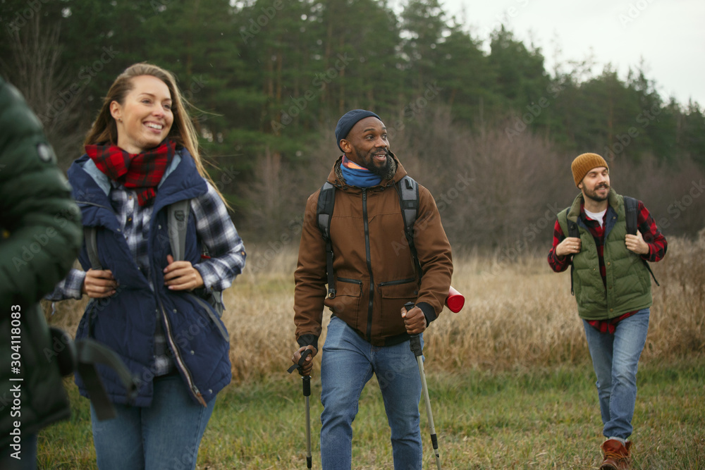 Group of friends on a camping or hiking trip in autumn day. Men and women with touristic backpacks going throught the forest, talking, laughting. Leisure activity, friendship, weekend. Group of friends on a camping or hiking trip in autumn day. Men and women with touristic backpacks going throught the forest, talking, laughting. Leisure activity, friendship, weekend.