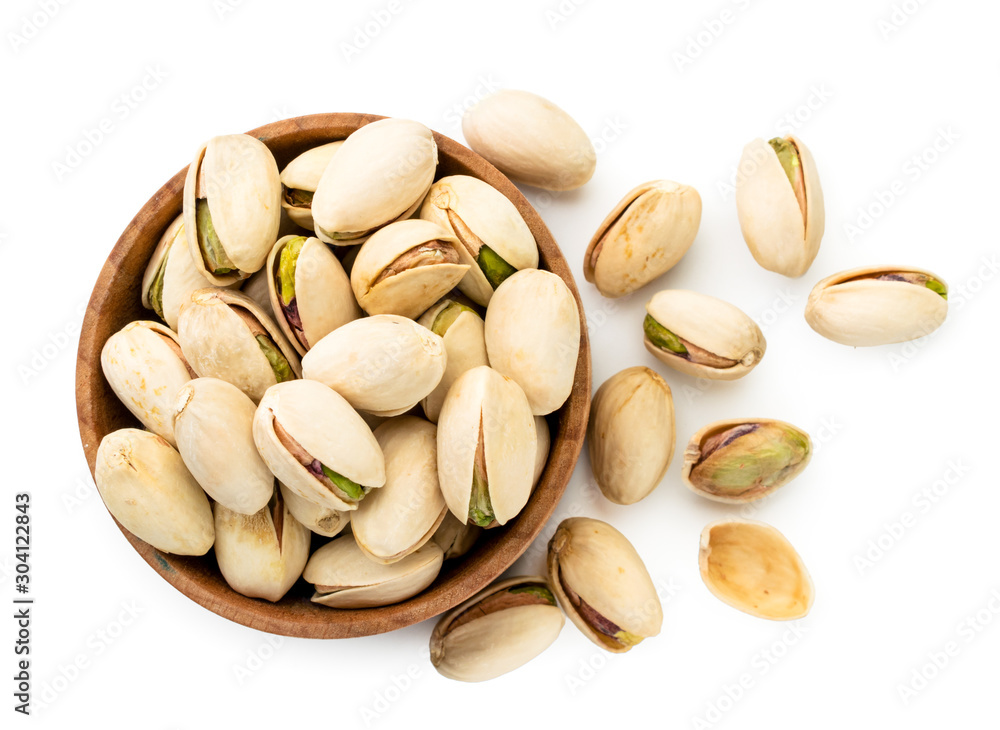 Pistachios spilled from a wooden plate on a white. The view of the top. Pistachios spilled from a wooden plate on a white. The view of the top.