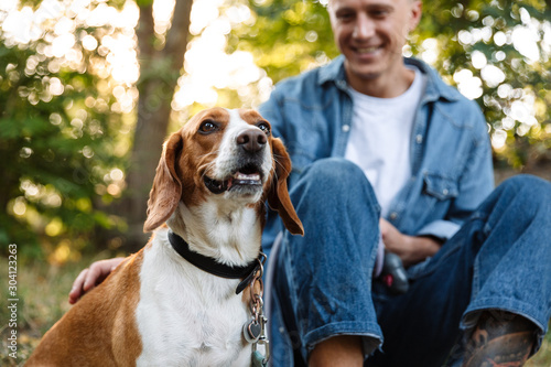 Canvas Print Photo of happy young man sitting on ground in park with his canine dog