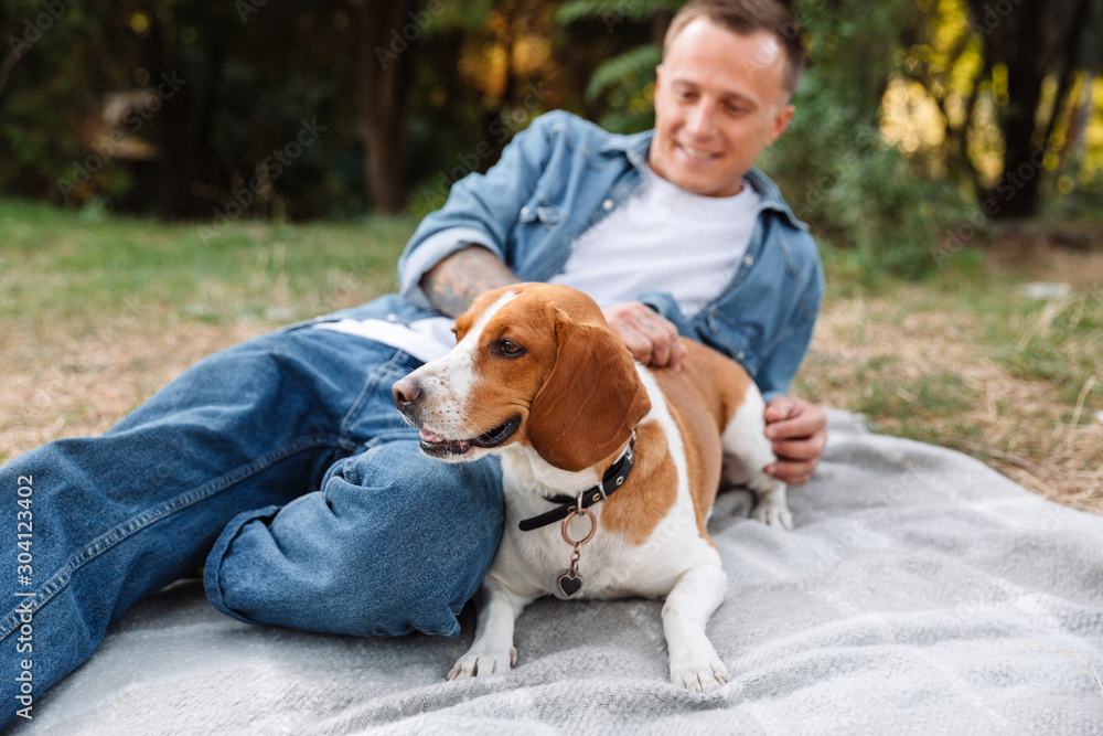 Photo of handsome young man sitting on blanket in park with his canine dog Photo of handsome young man sitting on blanket in park with his canine dog
