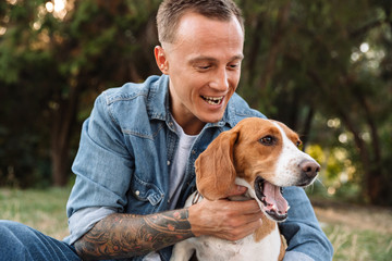 Photo of excited young man smiling and hugging his canine dog in park