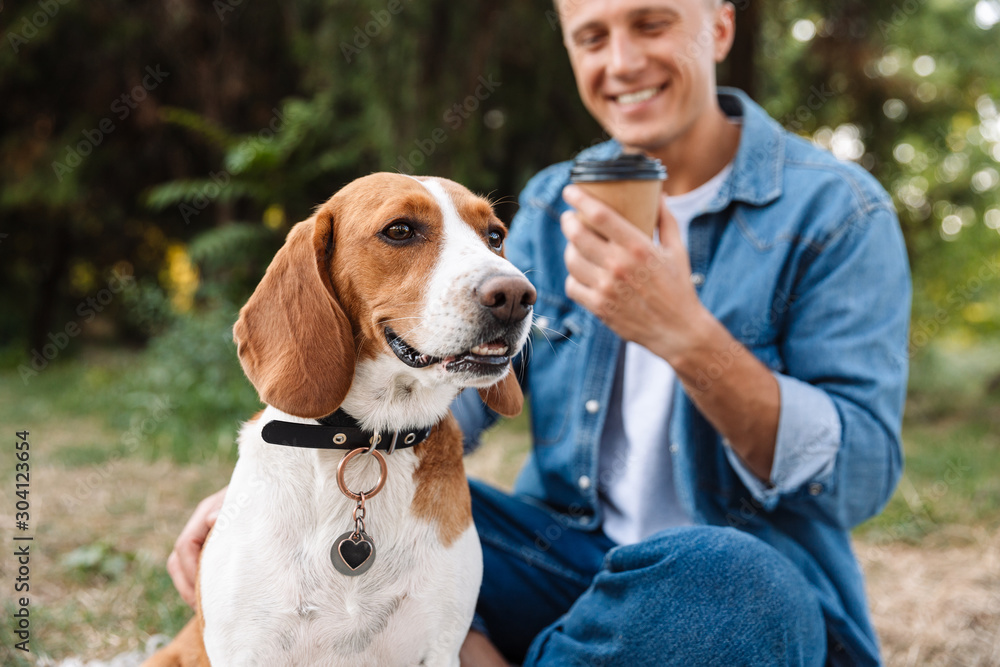 Photo of young man drinking coffee in park while walking with his dog