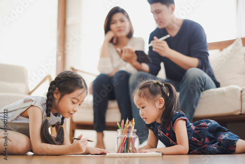 Young Asian family love  daughter sitting and laying on the wood floor in living room  education to writing and painting which smiling and felling happy near father and mother sit on sofa at home