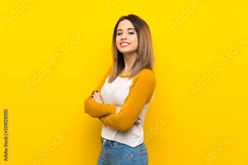 Pretty young woman over isolated yellow wall with arms crossed and looking forward