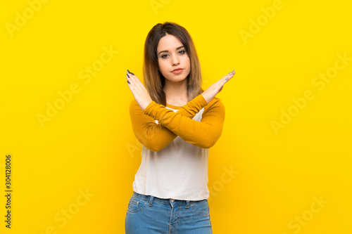 Pretty young woman over isolated yellow wall making NO gesture