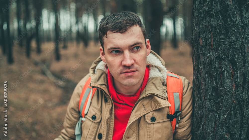 A traveling man with map in woods. A portrait of the handsome man with a backpack, standing near a tree in a cold weather. A traveling man with map in woods. A portrait of the handsome man with a backpack, standing near a tree in a cold weather.