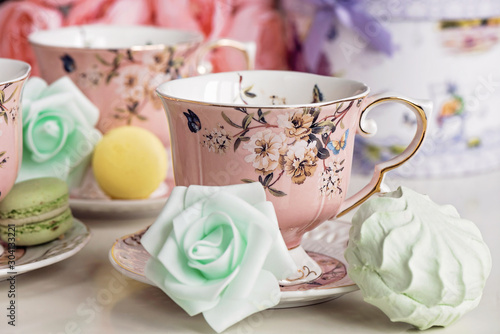 Pink tea cups with floral ornament and macaroon sweets
