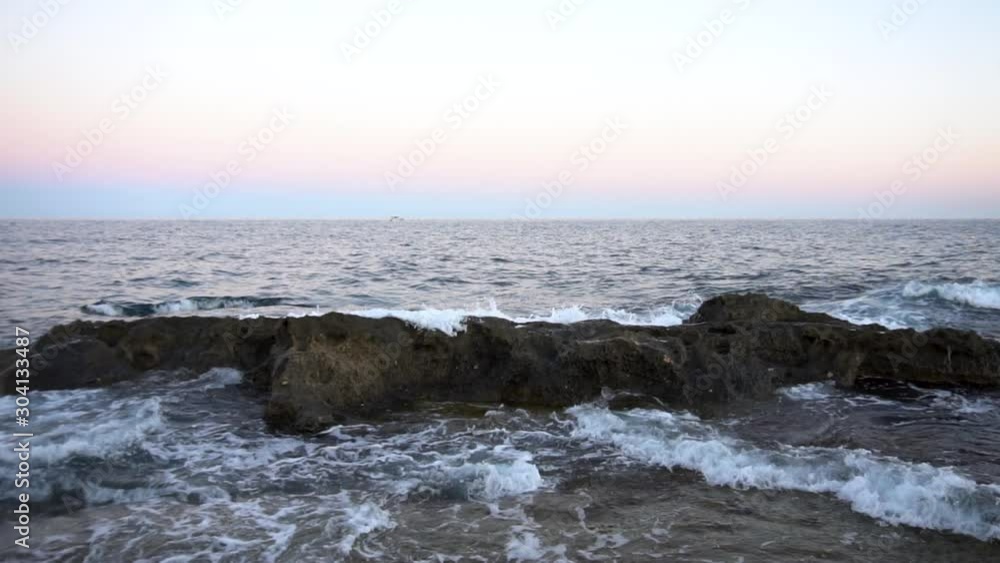 Waves on the Mediterranean Sea. Waves hit the rocks at pink sunset. Slow motion Waves on the Mediterranean Sea. Waves hit the rocks at pink sunset. Slow motion