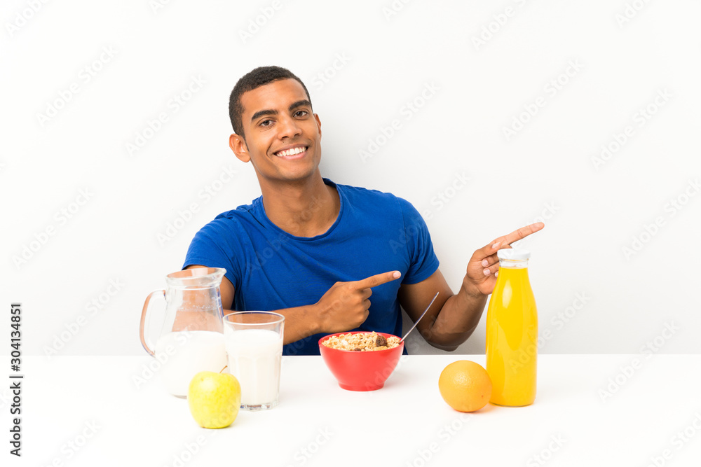 Young man having breakfast in a table pointing finger to the side Young man having breakfast in a table pointing finger to the side