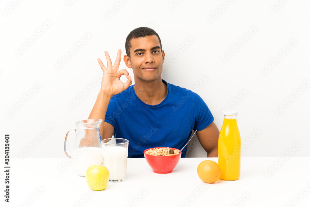 Young man having breakfast in a table showing an ok sign with fingers Young man having breakfast in a table showing an ok sign with fingers
