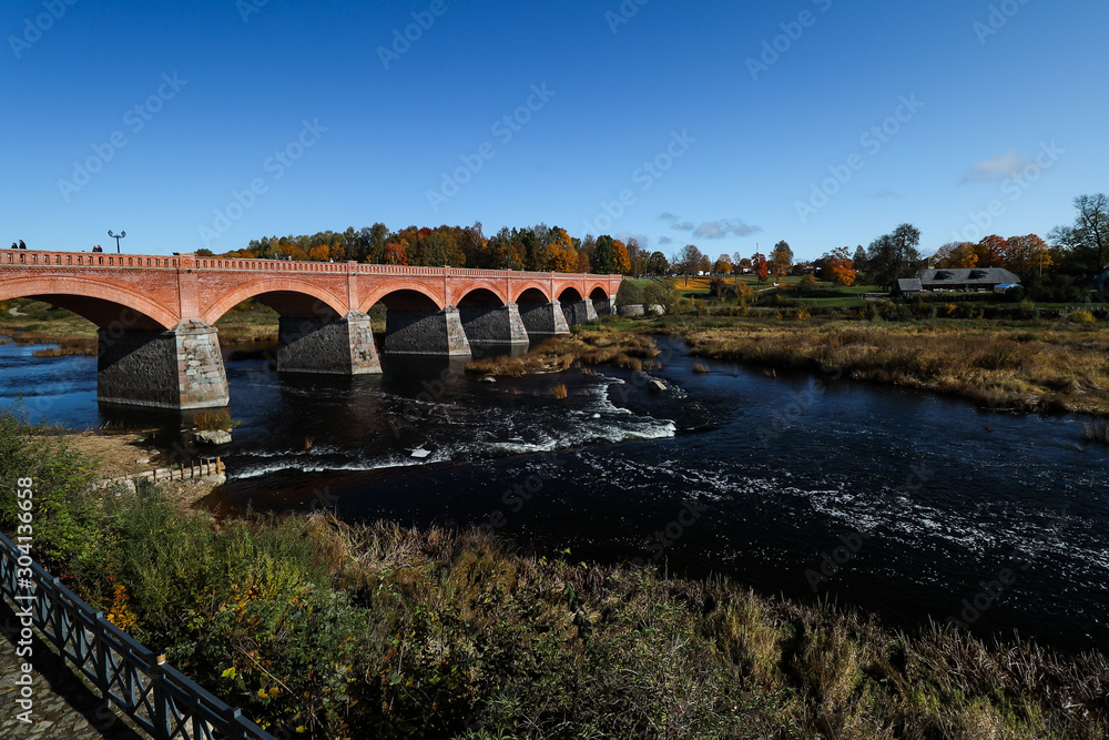 Daytime view of historic red brick bridge over river Venta in Europe-Latvia-Kuldīga.