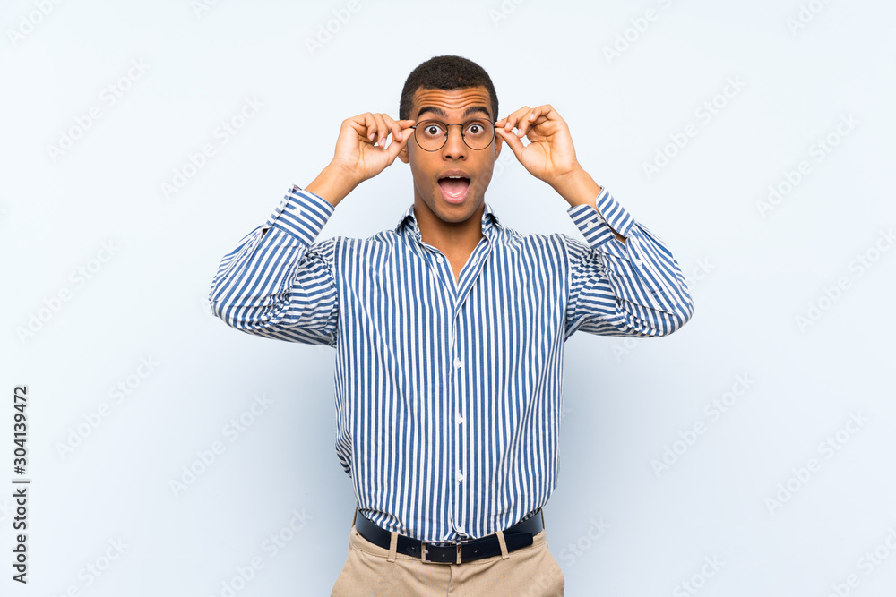 Fototapeta premium Young handsome brunette man over isolated blue background with glasses and surprised