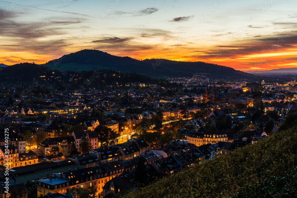 Germany, Freiburg im breisgau city skyline, cityscape and houses illuminated by night, decorated by magical red sunset sky, aerial view above roofs