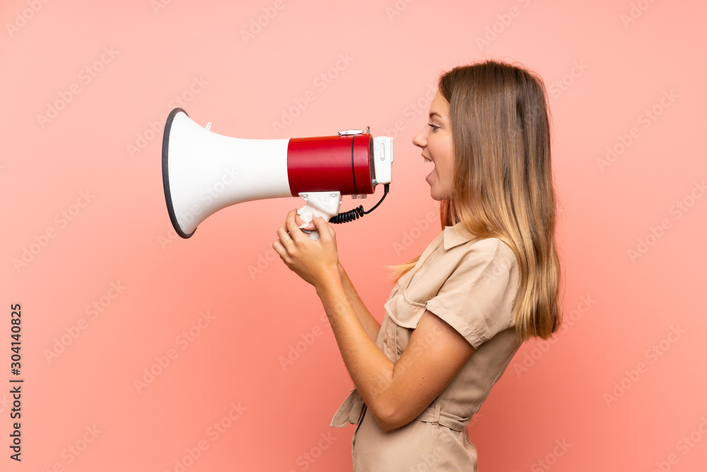 Lithuanian blonde girl over isolated pink background shouting through a megaphone Lithuanian blonde girl over isolated pink background shouting through a megaphone