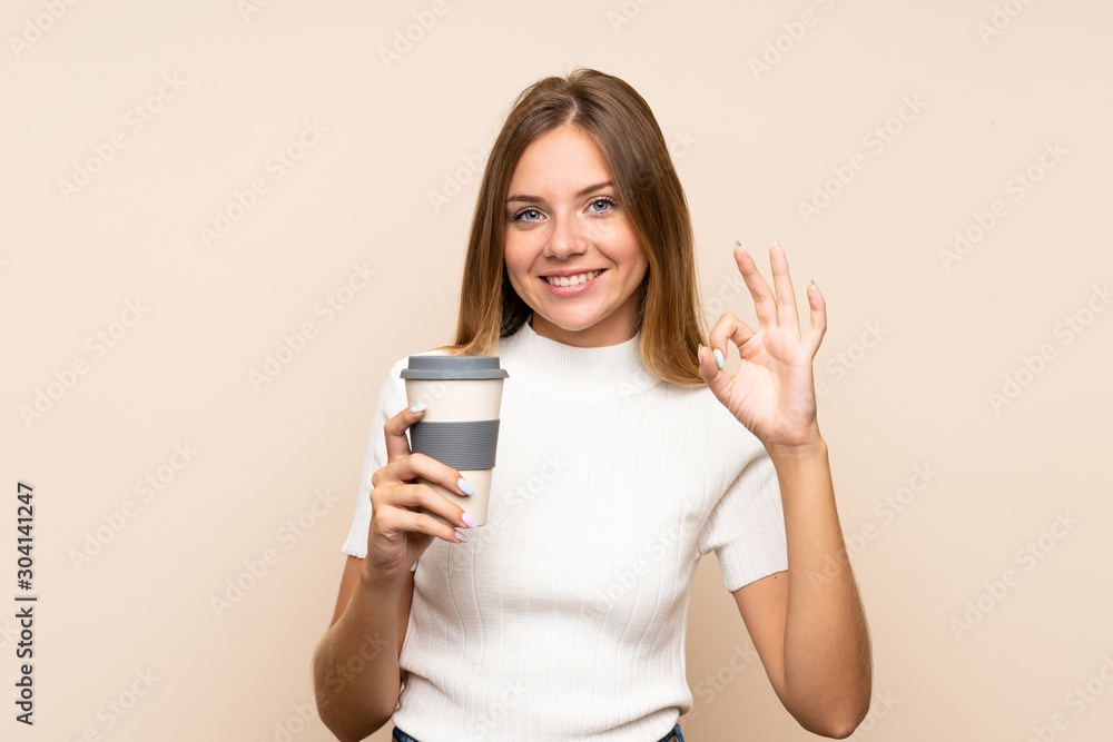 Young blonde woman over isolated background holding coffee to take away while making OK sign Young blonde woman over isolated background holding coffee to take away while making OK sign