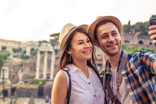 Young couple tourist looking at Roman Forum at sunrise and taking selfie. Historical imperial Foro Romano in Rome, Italy from panoramic point of view.