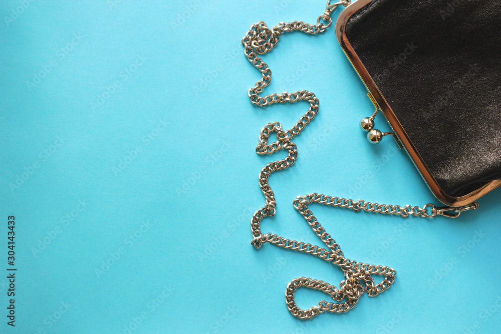 black women's clutch bag on a chain on a blue background, top view, copy space, flat lay black women's clutch bag on a chain on a blue background, top view, copy space, flat lay