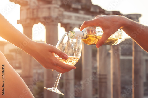 Canvas Print Pouring bottle of white wine in glasses at Roman Forum at sunrise
