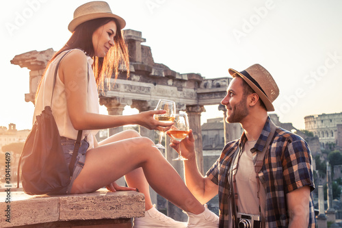 Photography Young couple tourist with glass of white wine at Roman Forum at sunrise