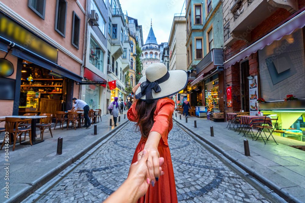 Women tourists holding man's hand and leading him to Galata tower in Istanbul, Turkey. - obrazy, fototapety, plakaty 