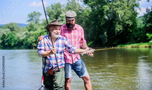 Fishing with spinning reel. Sunny summer day at river. Fisherman family. Hobby sport. Fishing peaceful activity. Father and son fishing. Rod tackle. Fishing equipment. Grandpa and mature man friends