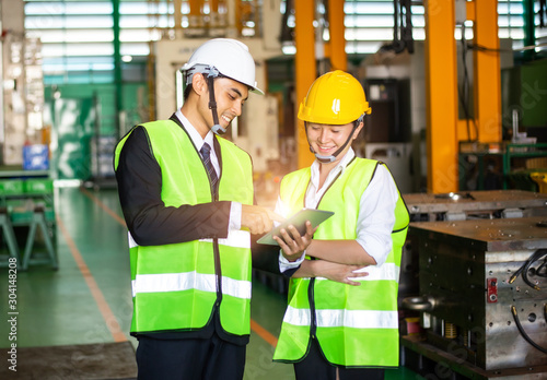 Businessmen or male engineers and female engineers are working in industrial plants that have machines and injection molds, with tablets used to control technology.
