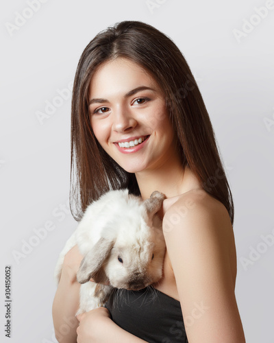 portrait of a young girl with a white pet rabbit in her arms. gray background