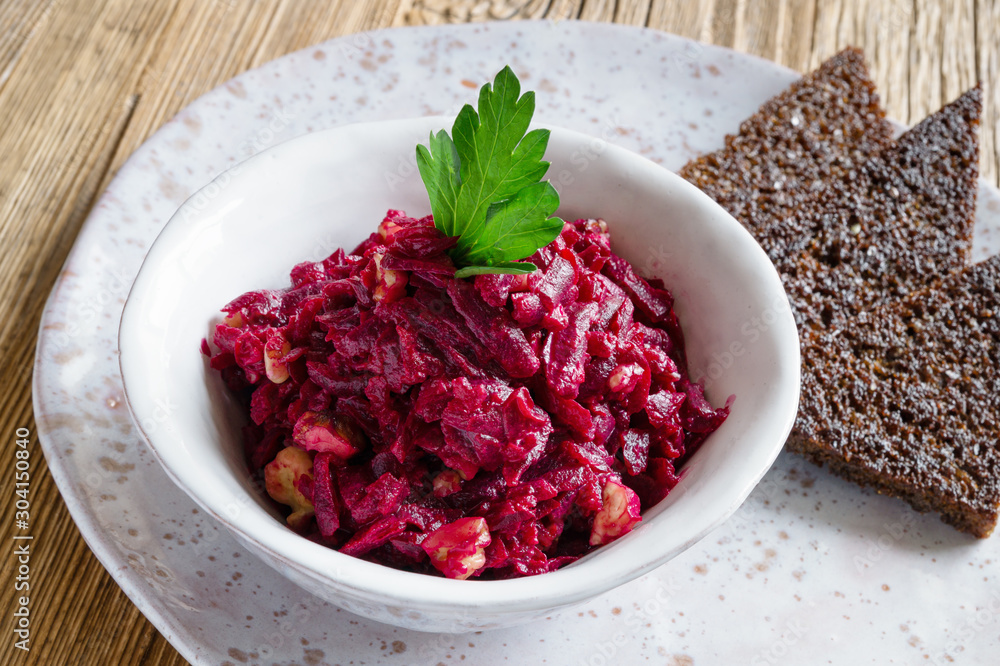 beetroot, walnuts, and garlic salad dressed with mayonnaise, decorated with parsley, and served with fried rye bread on a plate