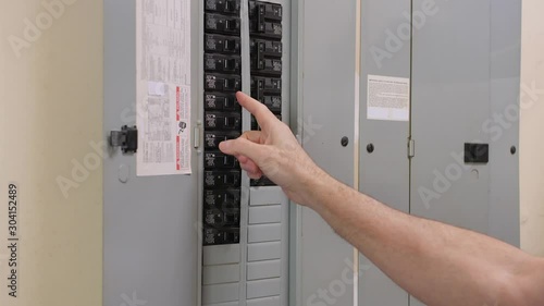 Male electrician turning off power for electrical outlet at circuit breaker box. Residential electricity power panel.