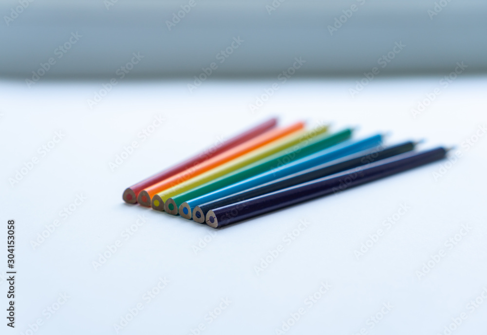 Fototapeta premium Set of seven sharp rainbow-colored pencils on a white background. Selective focus. Concept of creativity. Art supplies. Minimalism. Childhood.