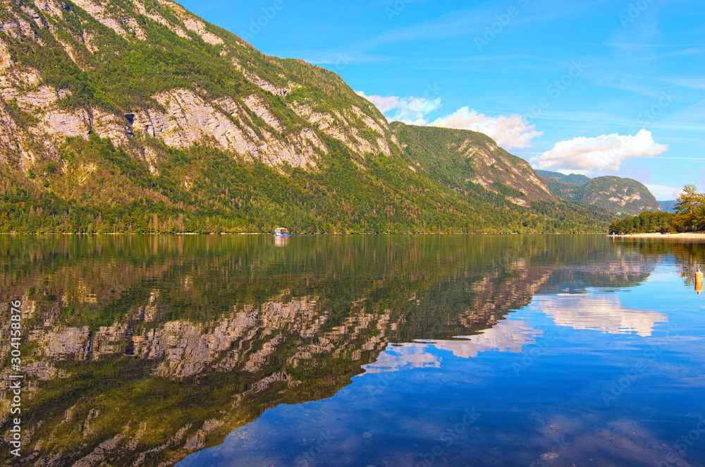 Panoramic view of Bohinj Lake with mountain range which reflected in turquoise water. Famous touristic place and travel destination in Europe. Bohinj Lake, Triglav National Park, Slovenia
