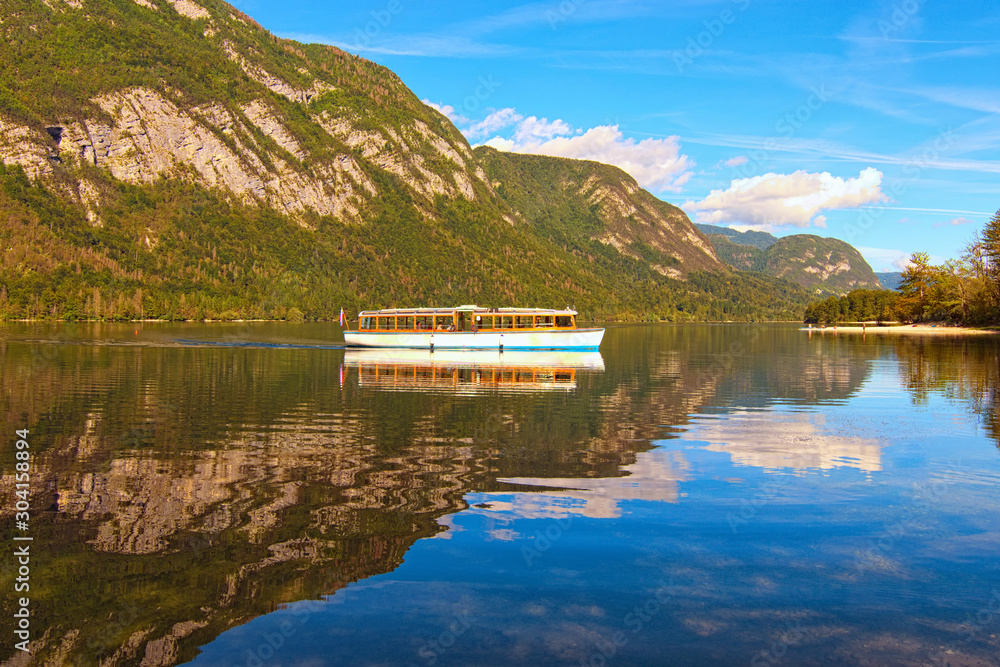 Fototapeta premium Old touristic boat on Bohinj Lake. Panoramic view of Bohinj Lake with mountain range which reflected in turquoise water. Romantic and peaceful scene. Bohinj Lake, Triglav National Park, Slovenia