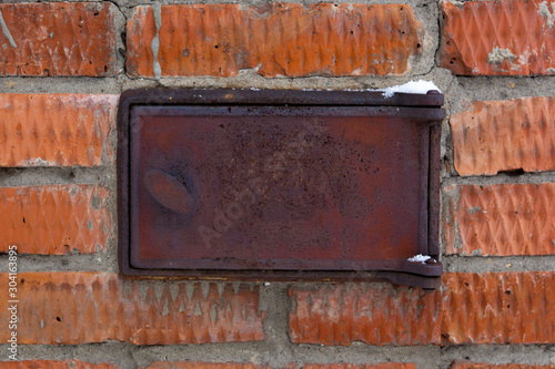 Abstract background in the form of an old brickwork of brown color and a metal stove rusty door close-up.