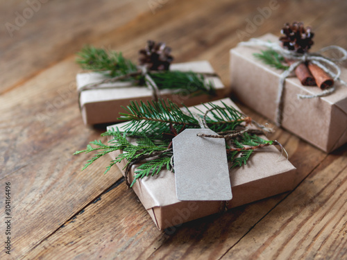Christmas presents wrapped in craft paper with natural fir tree and thuja branches as decoration. Wooden table with hand made New Year gifts.