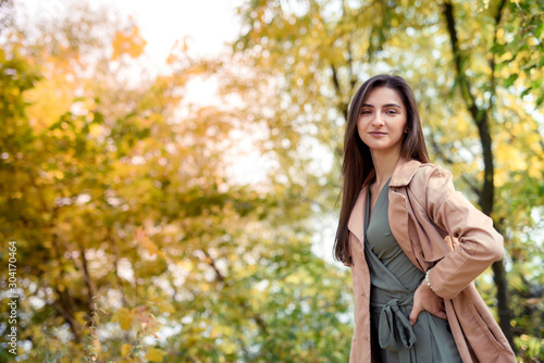 Autumn park. Beautiful woman in green dress posing in autumn park with yellow leaves