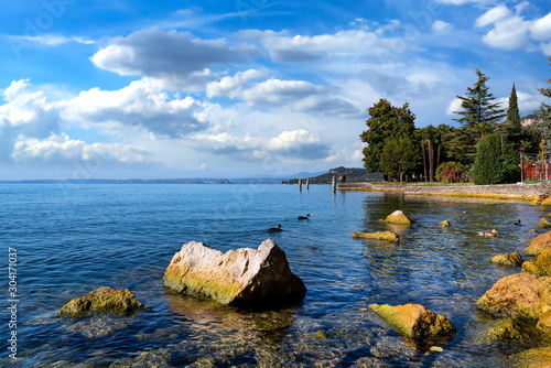 View to the beautiful boardwalk in Garda with crystal clear water and stones in foreground