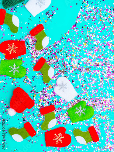 Colorful Sparkling holographic glitter confetti, toy hats, mittens, boots. Christmas Holidays abstract blue background