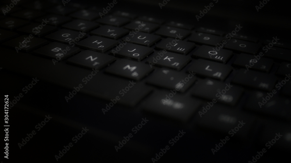 Black keyboard with white Roman alphabet and Cyryllic alphabet letters in the dark. Business concept